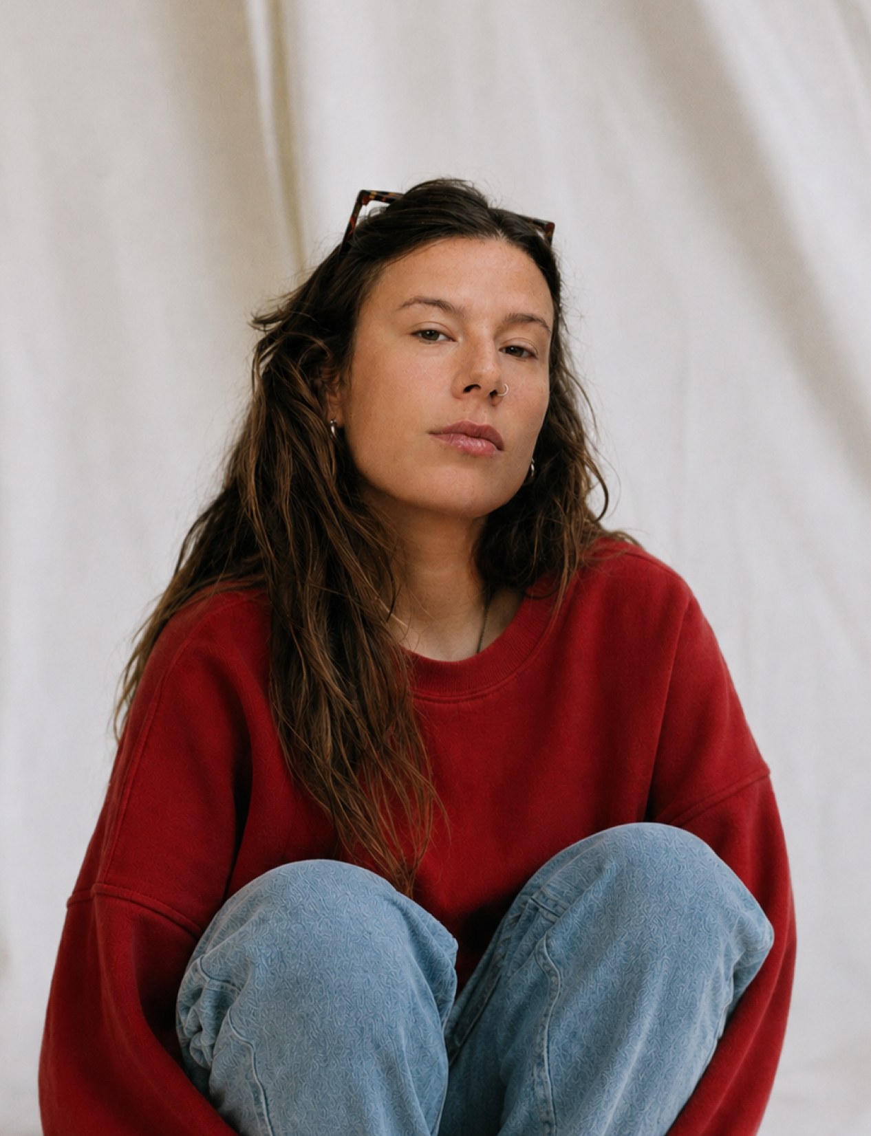 Portrait of Charlie Forster seated, wearing a red sweater, against a linen backdrop